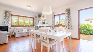 A spacious living area with a dining table, white furniture, and large windows. - Holiday Home "Es Viola" with Mountain Views, Pool, Wi-Fi, Garden and Terrace (Santa Eugènia)