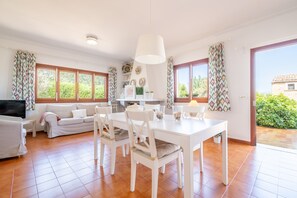 A spacious living area with a dining table, white furniture, and large windows. - Holiday Home "Es Viola" with Mountain Views, Pool, Wi-Fi, Garden and Terrace (Santa Eugènia)