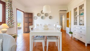 A dining area with a white table, chairs, a hanging light fixture, and a view through an open door. - Holiday Home "Es Viola" with Mountain Views, Pool, Wi-Fi, Garden and Terrace (Santa Eugènia)