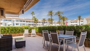 Une terrasse extérieure avec une table et des chaises, un canapé en osier et une vue sur un bâtiment d’hôtel bordé de palmiers.