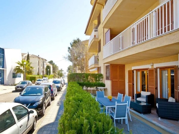 A residential building with a balcony, parked cars, and a small outdoor seating area.