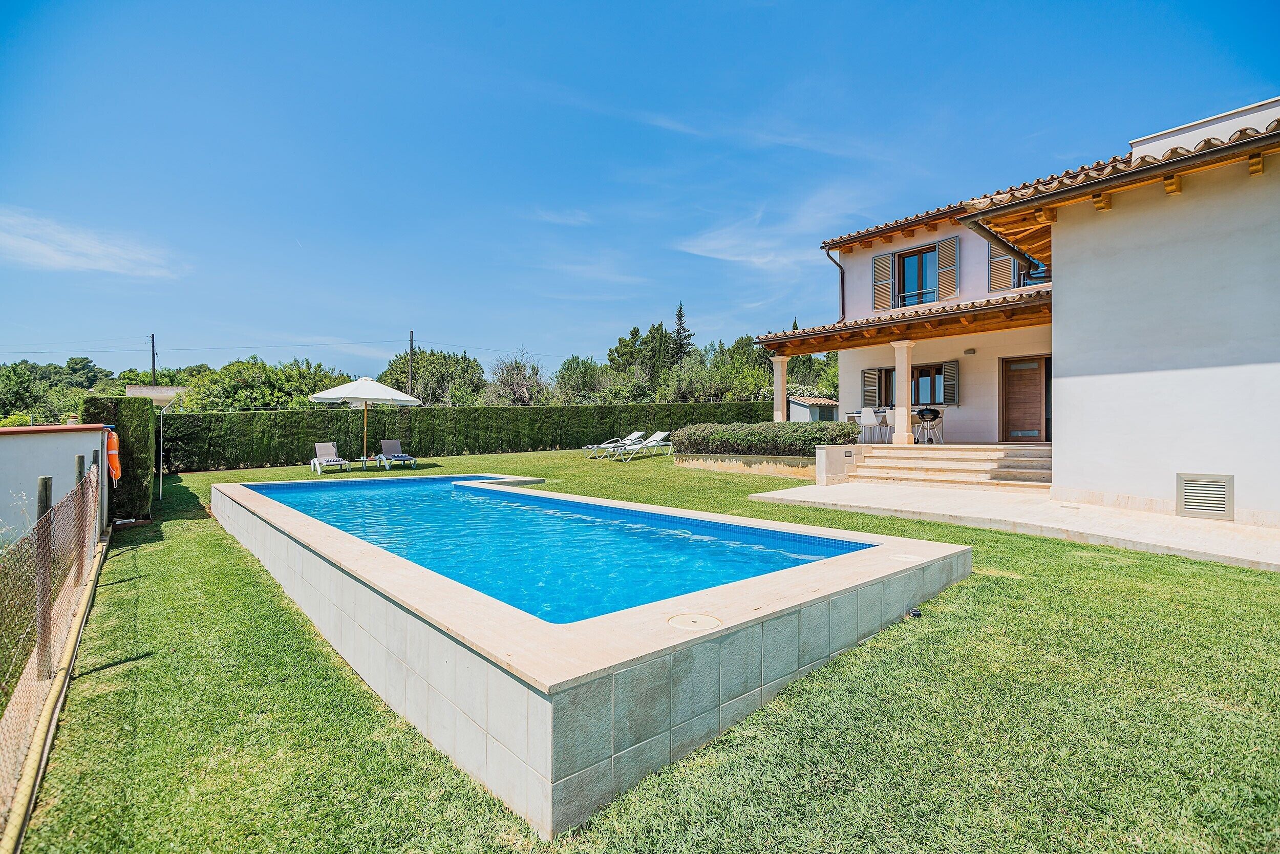 A swimming pool with a tiled deck, a grassy lawn, and a two-story house with a balcony.