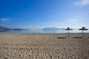 Una playa con arena, algunos paraguas y un mar tranquilo.