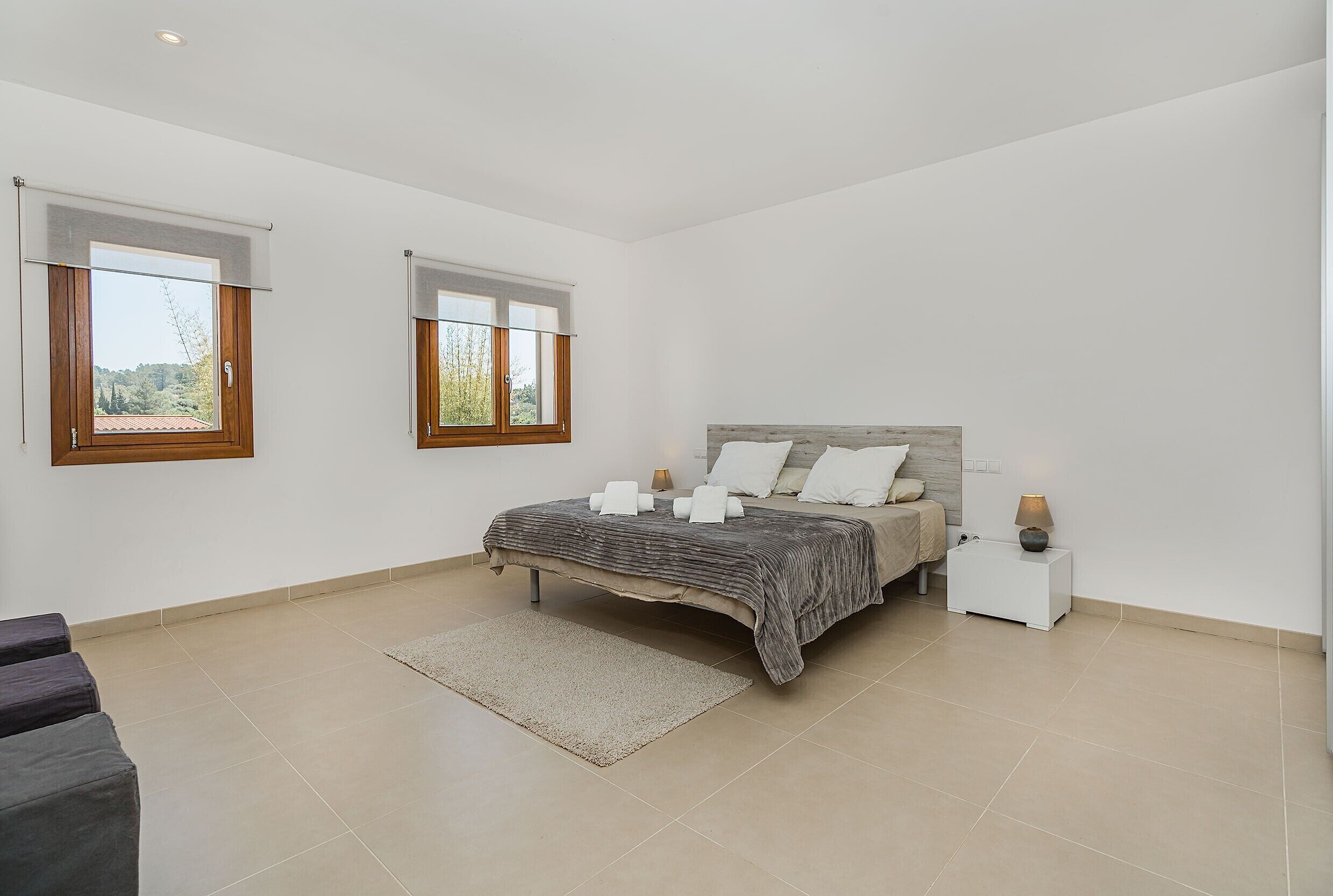 Une chambre à coucher avec un lit, deux tables de chevet, une fenêtre et une vue sur l’extérieur.
