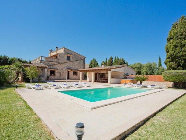 A two-story house with a swimming pool, lounge chairs, and a covered patio area.