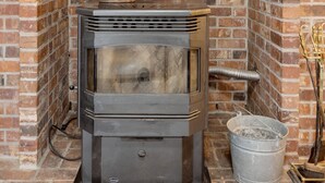 Un poêle à bois est installé dans une cheminée en briques, avec un tuyau métallique au-dessus et un seau en métal sur le côté droit.