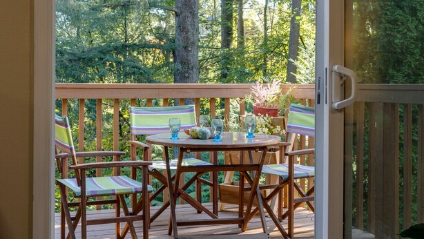 Une terrasse en bois avec une porte vitrée donnant sur une zone boisée.