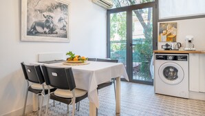 Un comedor con una mesa, sillas y una cesta de frutas. Se ve una lavadora y una cafetera al fondo.