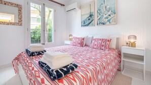 Un dormitorio con cama, mesita de noche, lámpara, espejo y dos cuadros en la pared.