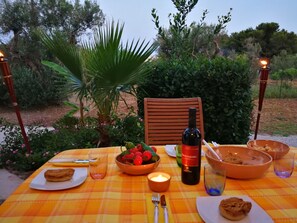 An outdoor dining table with a bottle of wine, bowls of food, and a candle. - Vacation Home Villetta Relax Salento close to the Sea with Terrace & Garden (Torre Suda)