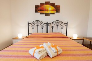 A bed with a striped bedspread, two bedside tables with lamps, and a wall-mounted artwork. - Vacation Home Villetta Relax Salento close to the Sea with Terrace & Garden (Torre Suda)