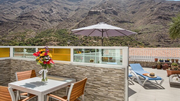 A terrace with a table, chairs, an umbrella, and a view of a mountainous landscape. - Apartment 'Casa Paco' with Mountain Views, Fast Wi-Fi, Air Conditioning and Terrace (Mogán)