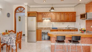 A kitchen with wooden cabinets, a refrigerator, a microwave, a sink, and a dining area with a table and chairs. - Apartment 'Casa Paco' with Mountain Views, Fast Wi-Fi, Air Conditioning and Terrace (Mogán)