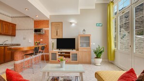 A modern living room with a TV, seating, a kitchen area, and a large window with a view. - Apartment 'Casa Paco' with Mountain Views, Fast Wi-Fi, Air Conditioning and Terrace (Mogán)