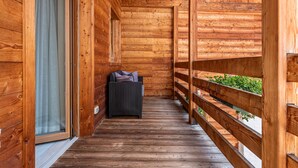 Un balcón de madera con una silla de mimbre y vistas a la vegetación.
