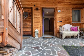 A wooden cabin entrance with a stone-tiled floor, a bench with pillows, and a lantern.