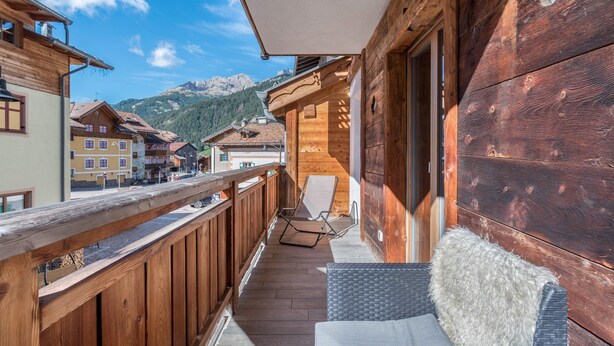 A wooden balcony with a wicker sofa and a chair, overlooking a mountain.