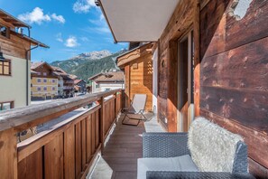 Ein Holzbalkon mit einer Rattan-Couch und einem Sessel, mit Blick auf einen Berg.