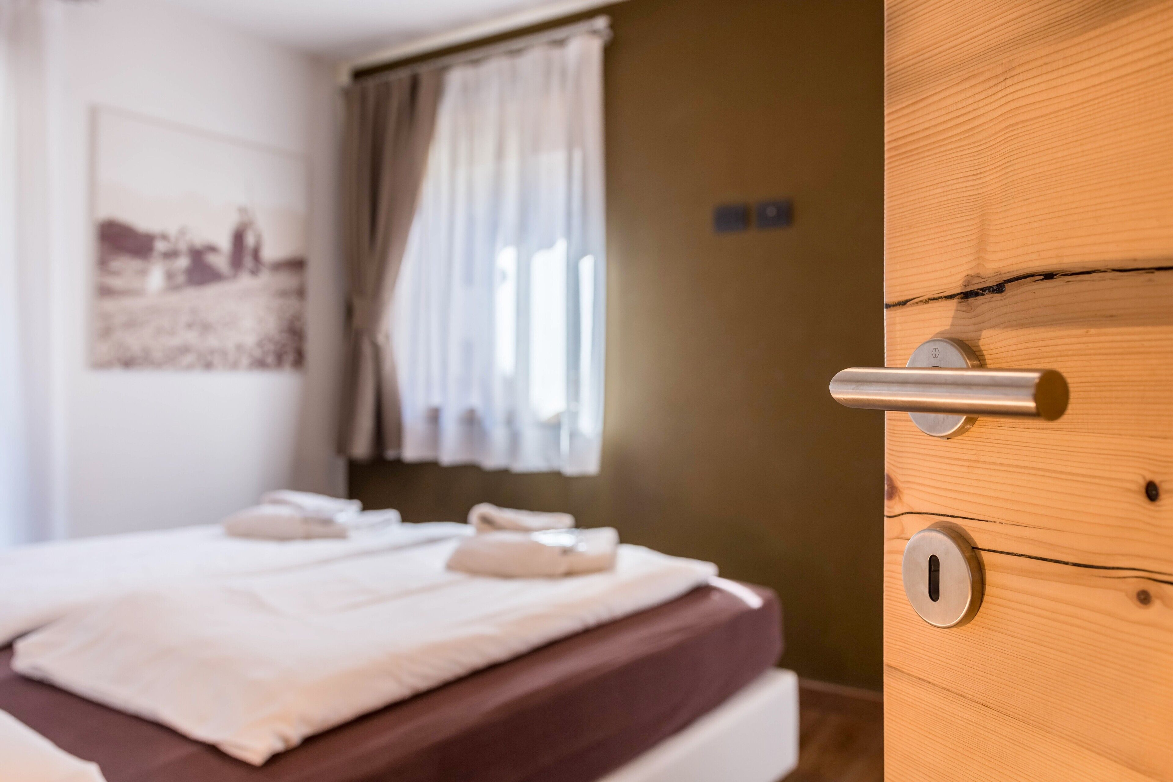 Una habitación de hotel con una cama, una puerta de madera y una ventana con cortinas.