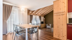 A modern kitchen with wooden cabinets, a dining table with chairs, and a lofted sleeping area.