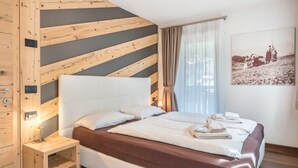 A bedroom with a bed, a nightstand, a wall-mounted light, a window with curtains, and a framed picture on the wall.