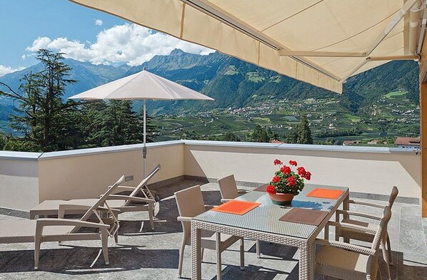 A terrace with outdoor furniture, a table with a flower centerpiece, and a mountain view. - Vacation Apartment "Sauvignon" with Mountain View, Wi-Fi, Balcony, Terrace & Garden (Meran)