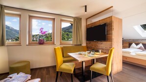 A modern room with a dining table, yellow chairs, a bed, a TV, and large windows with a mountain view. - Vacation Apartment "Barrique" with Mountain View, Wi-Fi and Garden (Meran)