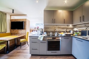 A modern kitchen with grey cabinets, a built-in oven, and a dining area with a yellow table and chair.