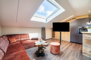 Een moderne woonkamer met een modulaire bank, een ronde tafel, een flatscreen televisie en een dakraam.
