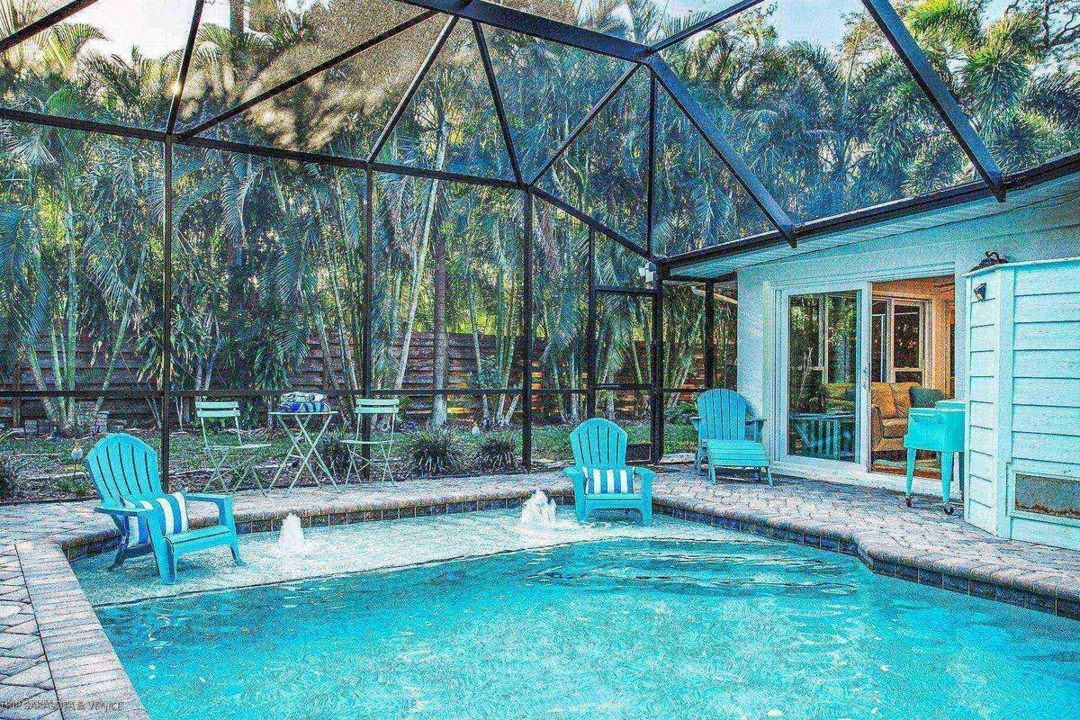 Una piscina con zona cubierta, rodeada de sillas y una casa con puerta y ventanas.
