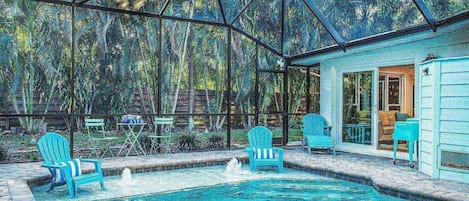 Una piscina con zona cubierta, rodeada de sillas y una casa con puerta y ventanas.