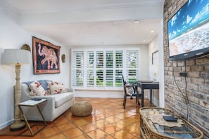 A living room with a sofa, a coffee table, a television, and a window with shutters.