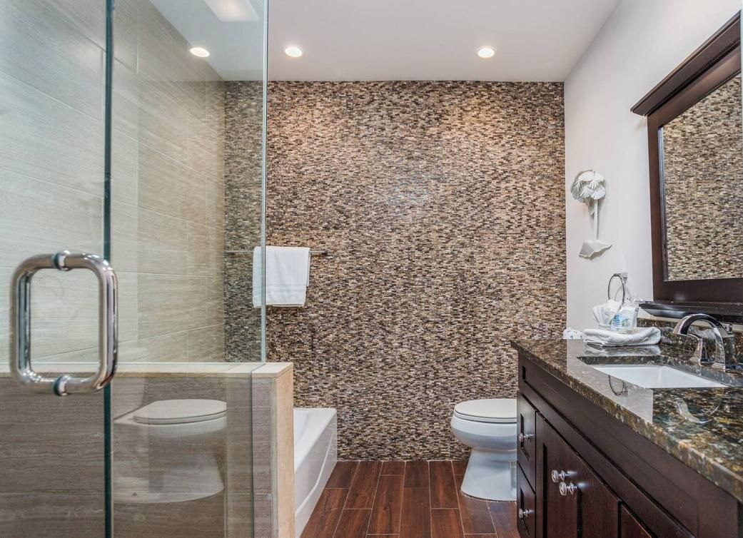 A bathroom with a glass shower enclosure, a white toilet, a bathtub, and a vanity with a mirror.