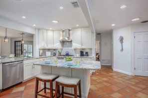 A kitchen with white cabinets, a central island with stools, a stove, and a sink.