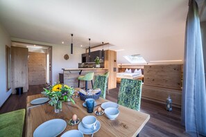 Un comedor moderno con una mesa de madera preparada para cuatro personas, un jarrón con flores y una cocina al fondo.
