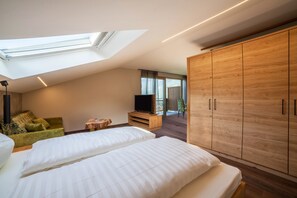 Une chambre moderne avec une lucarne, un téléviseur posé sur un meuble en bois, une armoire et un canapé vert.