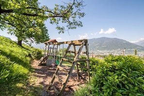 Un ensemble de balançoires en bois installé dans un parc, avec vue sur une ville et des montagnes en arrière-plan.