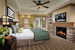 Cozy retreat with a large bed, fireplace, and TV, offering a peaceful view of the outdoors.