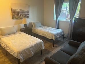 Two single beds with matching pillows and bedside lamps, a large painting, and a sofa in this inviting bedroom.