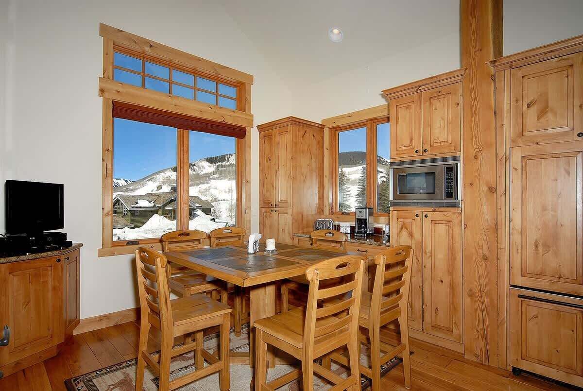 Cocina de madera con una mesa de comedor, sillas y vistas a montañas nevadas.