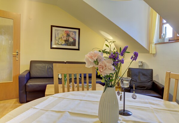 Et værelse med et spisebord, stole, en vase med blomster, et indrammet maleri og et vindue med gardiner.