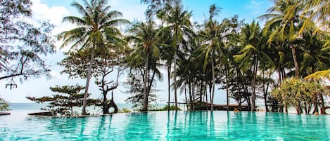 Una piscina infinita con agua turquesa cristalina, rodeada de palmeras y vista al océano.