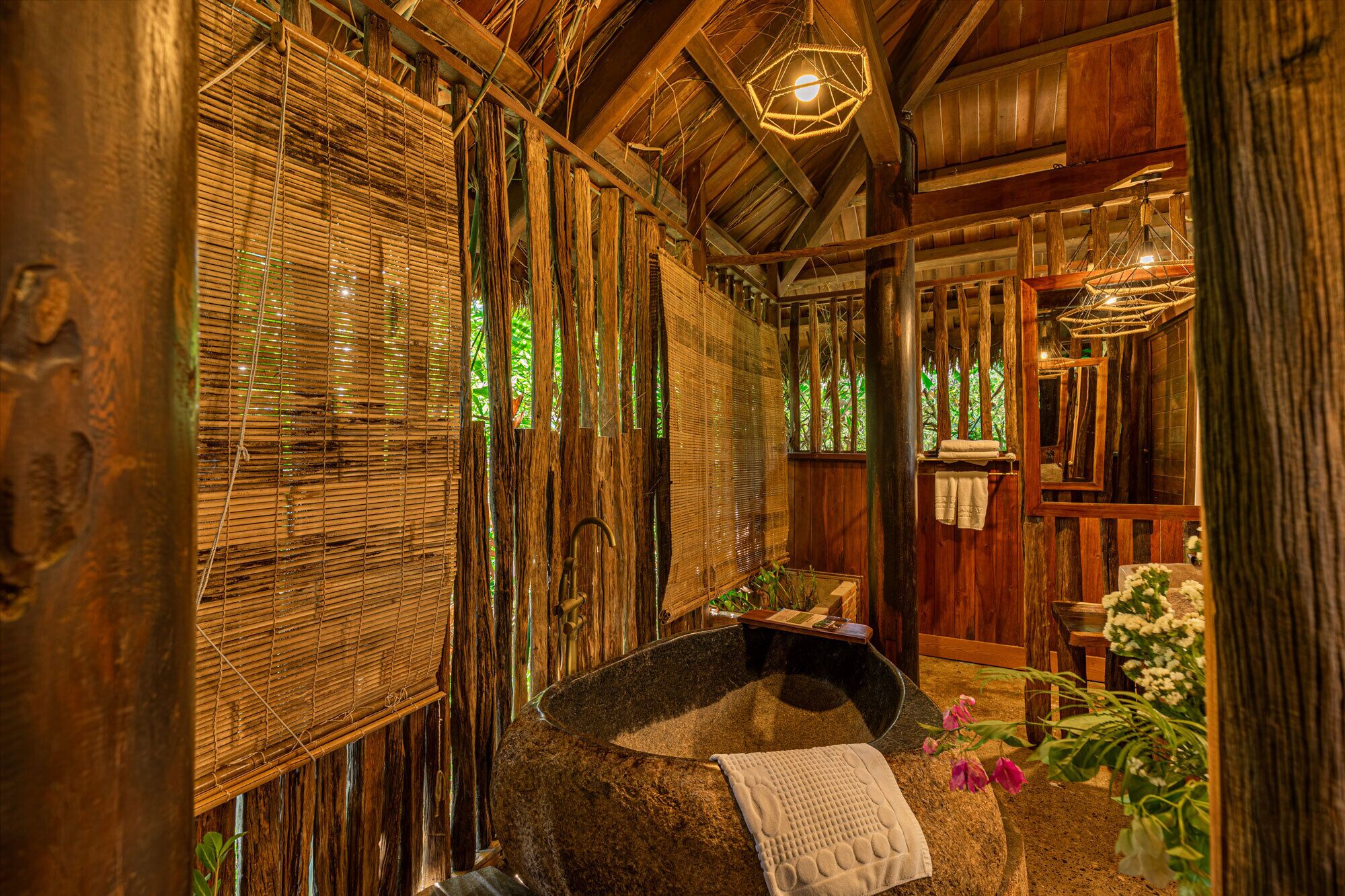 A rustic wooden room with a stone basin, bamboo blinds, and a hanging light fixture.