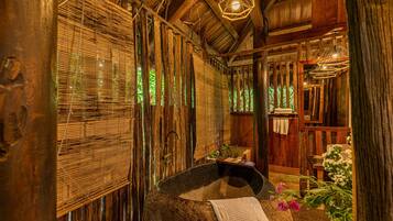 A rustic wooden room with a stone basin, bamboo blinds, and a hanging light fixture.
