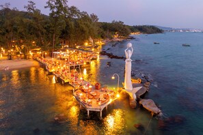 A waterfront restaurant with outdoor seating, a statue, and boats in the background. - Ocean Bay Phu Quoc Resort and Spa (Phu Quoc)