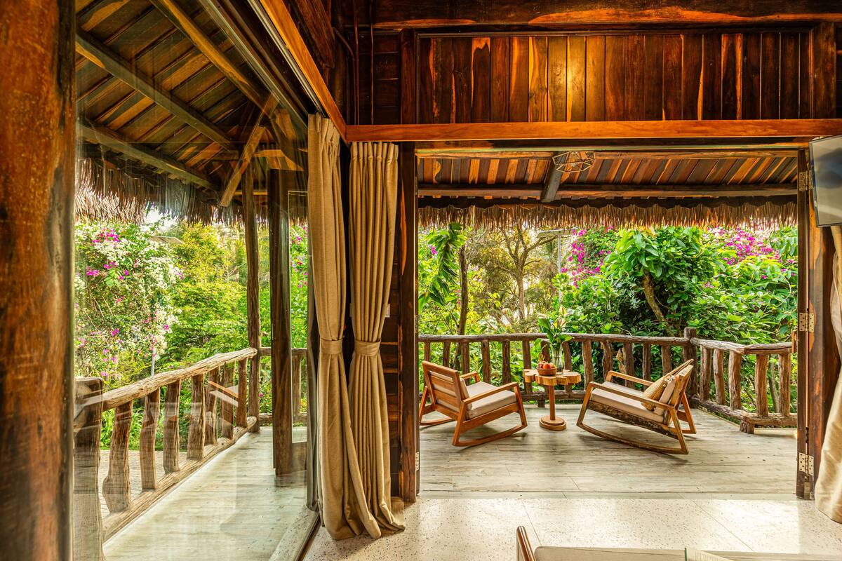 A wooden deck with a railing, two rocking chairs, and a table.