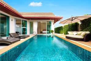 A swimming pool with lounge chairs and a sofa, surrounded by a house with large windows and a tiled roof. - Luxury Pool Villa A14 (Pattaya)