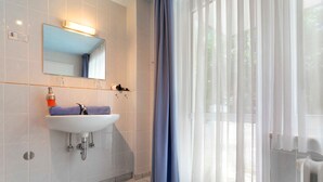 Een badkamer met een wit wastafel, spiegel en een raam met dunne gordijnen.