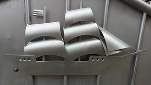Een metalen constructie met drie gebogen delen en een platte basis, mogelijk een decoratief object of onderdeel van een grotere installatie.