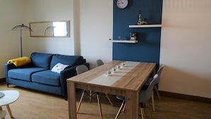 Een moderne woonkamer met een blauwe bank, een houten eettafel en een klok aan de muur.